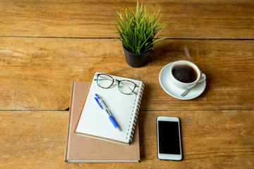 Coffee up and notebook, pen with glasses, cell phone on wooden table.