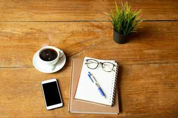 Coffee up and notebook, pen with glasses, cell phone on wooden table.