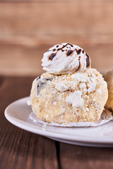 Two airy desserts with meringue in chocolate drops with prunes and butter cream in a white plate on a wooden background