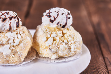Two airy desserts with meringue in chocolate drops with prunes and butter cream in a white plate on a wooden background
