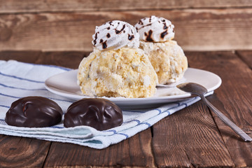 Two airy desserts with meringue in chocolate drops with prunes and butter cream and the chocolate zephyr in a white plate on a wooden background