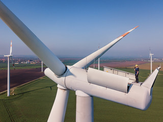 Aerial shot of a worker standing on the top of a wind turbine.