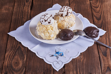 Two airy desserts with meringue in chocolate drops with prunes and butter cream and the chocolate zephyr in a white plate on a wooden background