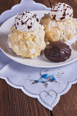 Two airy desserts with meringue in chocolate drops with prunes and butter cream and the chocolate zephyr in a white plate on a wooden background