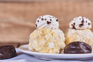 Two airy desserts with meringue in chocolate drops with prunes and butter cream and the chocolate zephyr in a white plate on a wooden background