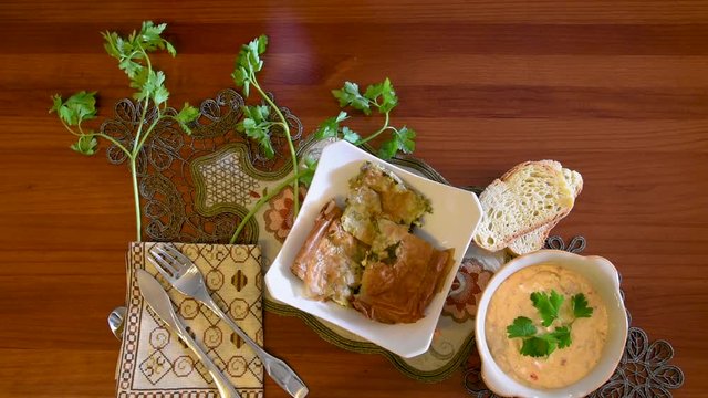 Healthy mediterranean cuisine, three dishes concept for lunch or dinner. Closeup of placing the letuce salad and a tomato on the table in slow motion