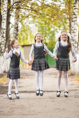 Smiling young children in a school uniform jumping on the road in the park at the day time.