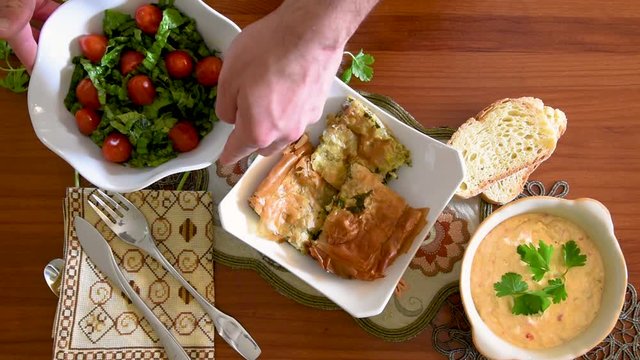 Healthy mediterranean cuisine, three dishes concept for lunch or dinner. Overhead closeup of placing the letuce salad with both hands on the table