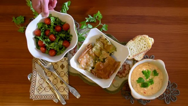 Healthy mediterranean cuisine, three dishes concept for lunch or dinner. Overhead closeup of placing the letuce salad with one hand on the table