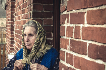 old woman in a sling in front of a brick house.