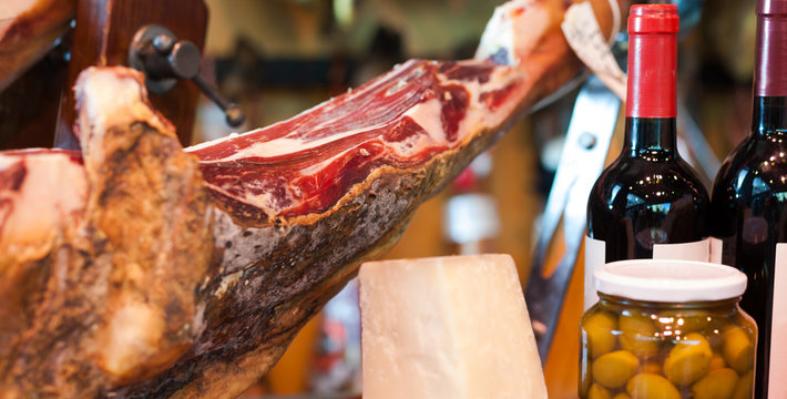 Still life of spanish pork jammon on holder, bottles of wine cheese and olives