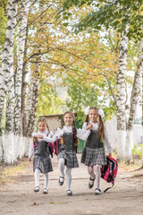 Smiling young children in a school uniform run and bounce happily on the road in the park