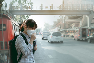 A student asian girl wearing PM 2.5 dust mask are in a city full of dust and smoke.