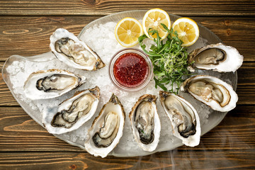 Fresh opened oysters, lemon, herbs, ice on a wooden table, top view.