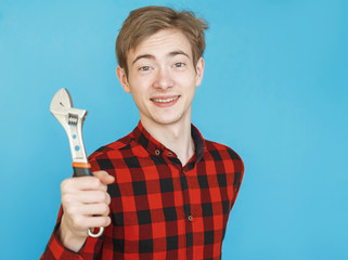 young serious male teenager in red shirt on blue background with tools . wrench