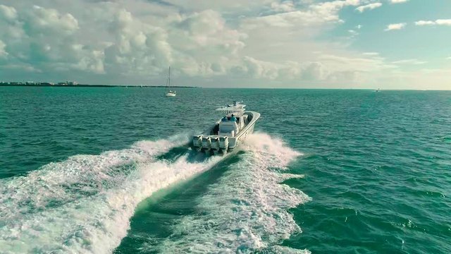 Aerial Quad Engine center console boat cruising speed with Sailboat in background in blue coastal waters