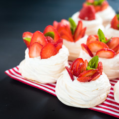 Strawberry pavlova cake nests, with mint on black table