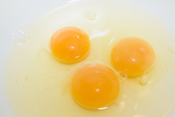 Three broken chicken eggs in a white mixing bowl