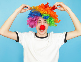 young funny male teenager in white t-shirt on blue background in clown wig