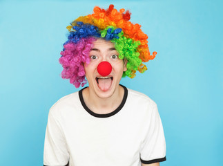 young funny male teenager in white t-shirt on blue background in clown wig