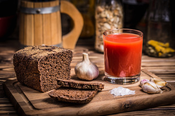 A glass of tomato juice on a wooden board with rye bread