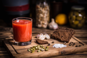 A glass of tomato juice on a wooden board with rye bread