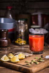 A glass of tomato juice on a wooden board with lemon slices, salt and pumpkin seeds.
