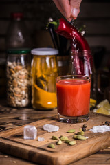 A hand pours salt into a glass of tomato juice on a wooden board with spices, salt and pumpkin seeds.