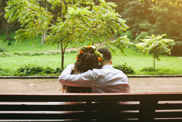 Fototapeta premium Wedding couple in love is sitting on the bench in the park. Bride and groom are hugging. Romantic concept.Warm summer day outdoors.