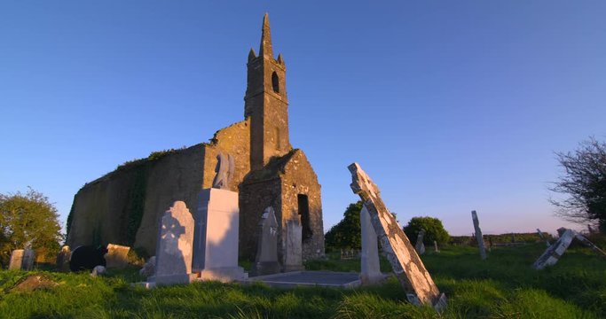 Ancient Irish church building ruin and graveyard headstones summer evening sunset