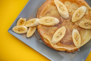 Stack of traditional russian pancakes blini with bananas and honey on yellow background. Homemade russian thin pancakes blini. Russian food, russian kitchen.
