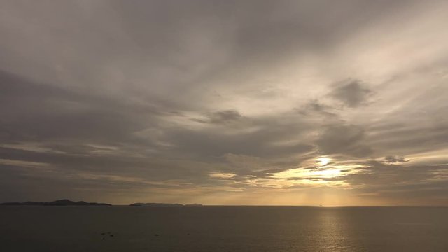 Timelapse of sunrise / sunset in the sea with moving clouds and a coast at the horizon