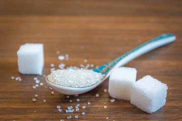 Some sugar cubes kept on a clean wooden floor. Sugar taken out from a bowl with a spoon. Copy space provided