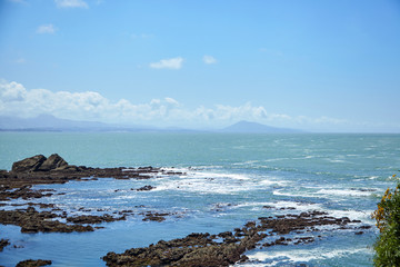 Fototapeta na wymiar Seascape. Waves with white foam, sharp stones and blue sky with clouds. Rocky Atlantic ocean coast
