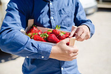 Person holding bag with healthy nutritious strawberries on groceries shopping market background,...