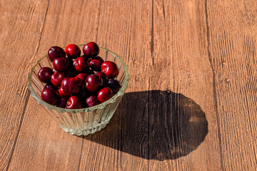 Berries of a sweet cherry in a glass bowl on a wooden background. Ripe red sweet cherry
