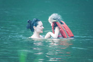Swimming lessons - woman is training to swim a girl in a life jacket