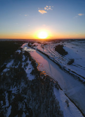 The forest and the frozen river with the appearance of thawed patches in the spring at sunset, when there is still snow in Russia from the height