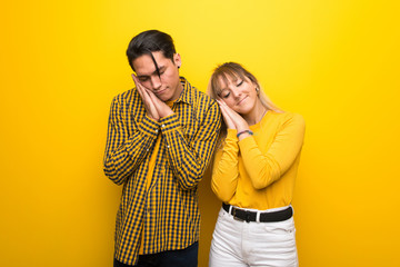 Young couple over vibrant yellow background making sleep gesture in dorable expression