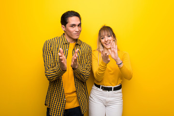 Young couple over vibrant yellow background applauding after presentation in a conference