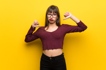 Woman with glasses over yellow wall showing thumb down