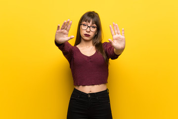 Obraz premium Woman with glasses over yellow wall making stop gesture and disappointed