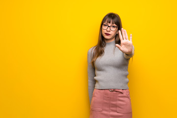 Woman with glasses over yellow wall making stop gesture denying a situation that thinks wrong