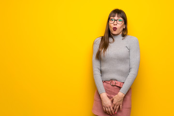 Woman with glasses over yellow wall with surprise and shocked facial expression