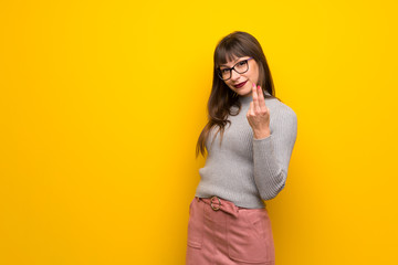 Woman with glasses over yellow wall inviting to come with hand. Happy that you came