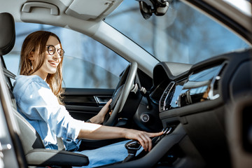 Young woman controlling air conditioner, touching the dashboard of the modern car in the city
