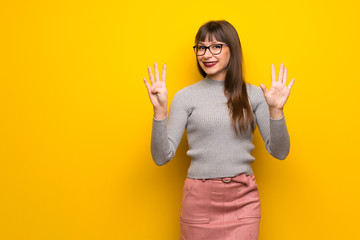 Woman with glasses over yellow wall counting nine with fingers