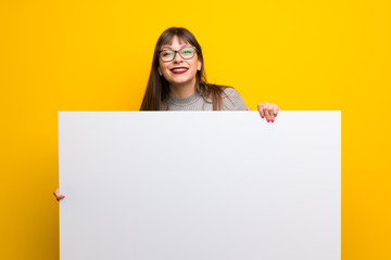 Woman with glasses over yellow wall holding an empty white placard