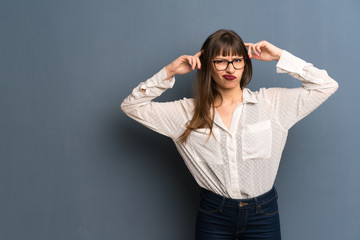 Woman with glasses over blue wall having doubts and thinking