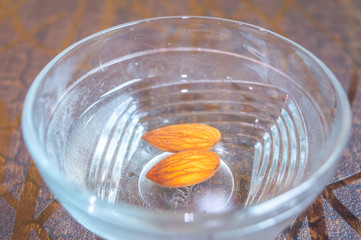 Fototapeta na wymiar Almonds kept in a glass bowl containing water. Peeling of almond skin in progress